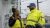 Two bp team members wearing yellow safety vests stand outside of a bp gas station in New York