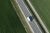 Aerial view of a white delivery van speeding on the road between green fields in spring.